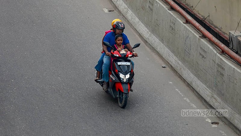 Three people, including a child, are on the same motorcycle on a busy road in Dhaka. While the driver and rear passenger are wearing helmets, the child seated in front is not. Photo: Mahmud Zaman Ovi
