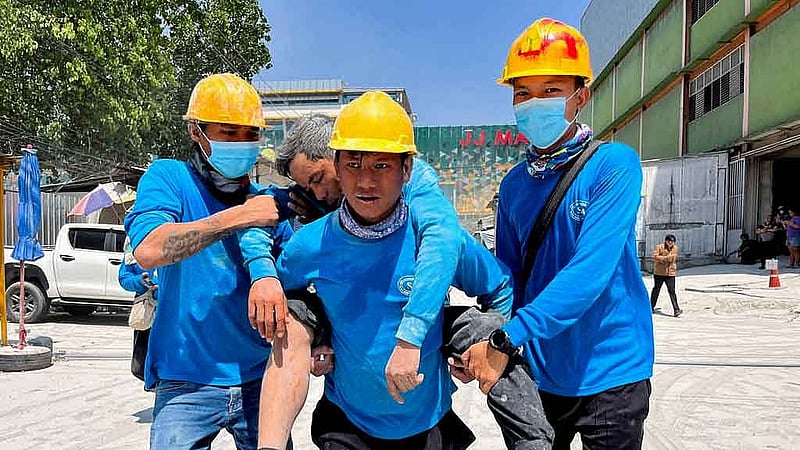 Workers carry an injured person near the site of a collapsed building after a strong earthquake struck central Myanmar on Friday, earthquake monitoring services said, which affected Bangkok as well with hundreds of people pouring out of buildings in the Thai capital in panic after the tremors, in Bangkok, Thailand, March 28, 2025. REUTERS
