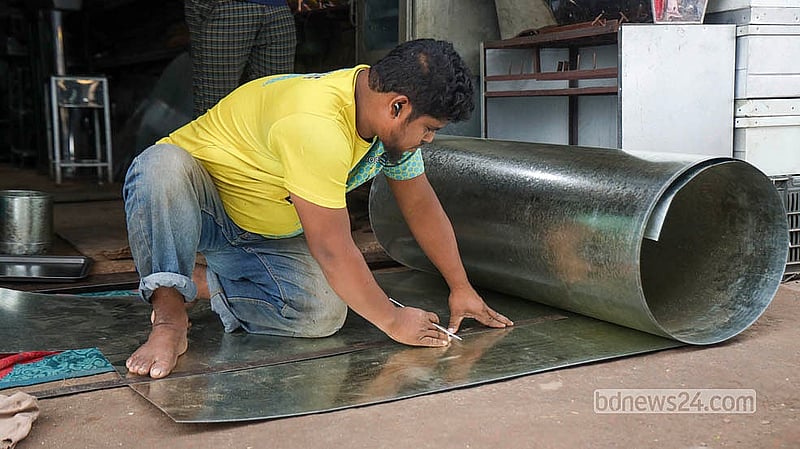 A craftsman measures black sheet metal before shaping it into a tin trunk at a workshop in Dhaka's Karwan Bazar.  Photo: Shamsul Hoque Ripon