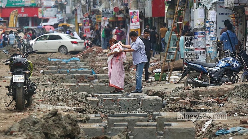 Repair work crawls along the Khilgaon-Basabo road as an elderly woman, apparently unwell, is helped along by another person.   Photo: Shamsul Haque Ripon