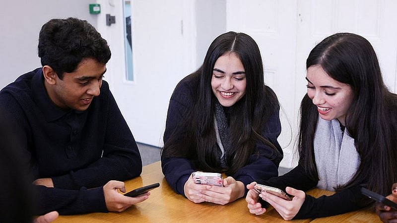 Students from Ricards Lodge High School in Wimbledon look at their mobile phones in London, Britain. REUTERS