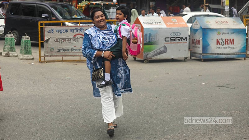 A mother carries her child across the road at Malibagh despite a footbridge being available for safe passage. Photo: Shamsul Haque Ripon