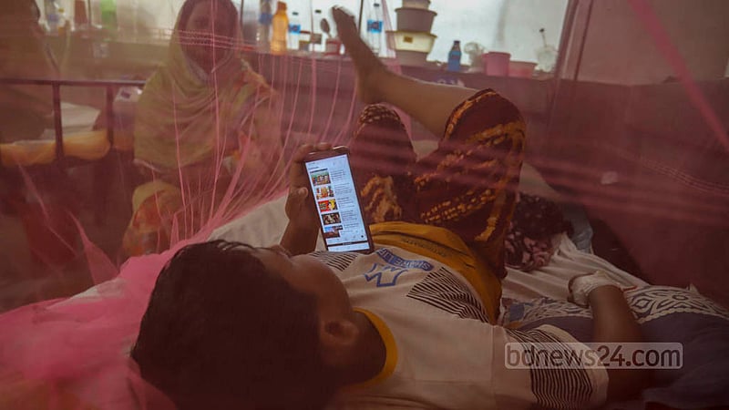 ঢাকার শিশু হাসপাতালে ডেঙ্গু জ্বরে আক্রান্ত এক শিশুর সময় কাটছে মোবাইলে।