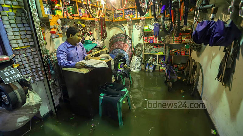 টানা বৃষ্টিতে পুরান ঢাকার বংশালের রাস্তা ছাপিয়ে দোকানেও ওঠে পানি। তার মধ্যেই দোকানে চলে বেচাকেনা।