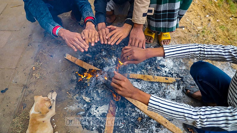ঢাকার হাতিরঝিলে শীত থেকে বাঁচতে ফুটপাতের পাশে আগুন জ্বালিয়ে উষ্ণতা পোহাচ্ছেন কয়েকজন তরুণ। ঠাণ্ডার কারণে তাদের পাশে এসে বসেছে একটি কুকুর ছানা।&amp;nbsp;ছবি: মাহমুদ জামান অভি