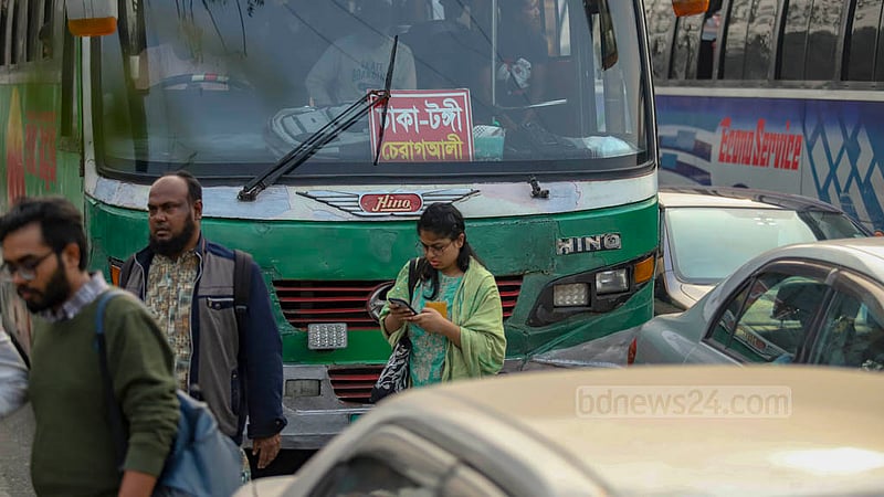ঢাকার রামপুরা ব্রিজের ব্যস্ত সড়ক পার হচ্ছেন এই নারী, পেছনেই বাস কিন্তু তার মনোযোগ মোবাইল ফোনে।&amp;nbsp;ছবি: মাহমুদ জামান অভি
