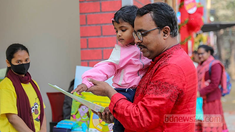 একুশে বইমেলায় শনিবার দ্বিতীয় শিশুপ্রহরে একটি স্টলে বাবার সাথে বই দেখছে এক শিশু। ছবি: আসিফ মাহমুদ অভি