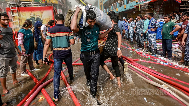 নিউ সুপার মার্কেটে আগুন লাগার পর নেভানোর কাজ করছে ফায়ার সার্ভিসের কর্মীরা; অন্যদিকে দোকানের মালামাল সরাতে সাহায্য করছে আইনশৃঙ্খলা বাহিনী।&amp;nbsp;ছবি: তাওহীদুজ্জামান তপু