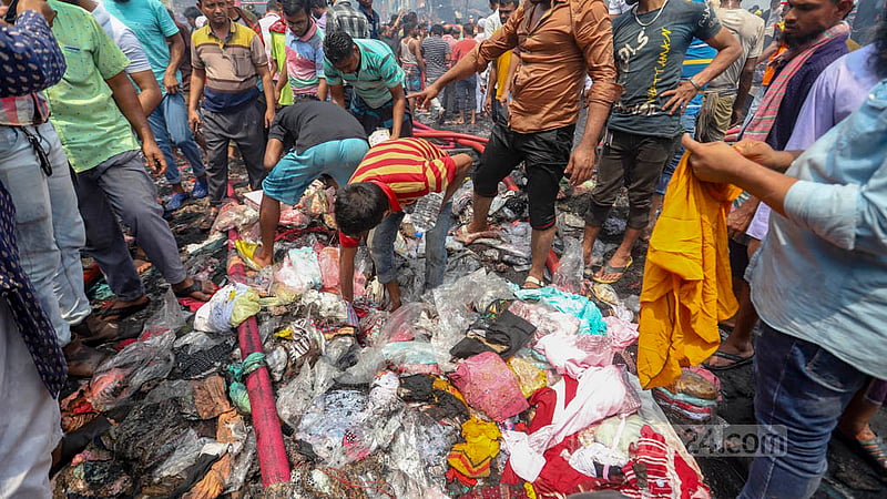 ভয়াবহ আগুন নিভে আসার পর শুরু হয় আরেক বিপদ; ঢাকার বঙ্গবাজারের পোড়া দোকানগুলোতে ‘হরিলুটে’ নেমে পড়ে দুবৃত্তরা। পোড়া আর পানিতে ভেজা কাপড়ের স্তূপ থেকে যে যেভাবে পেরেছে তা নিয়ে যায়।&amp;nbsp;ছবি: মাহমুদ জামান অভি