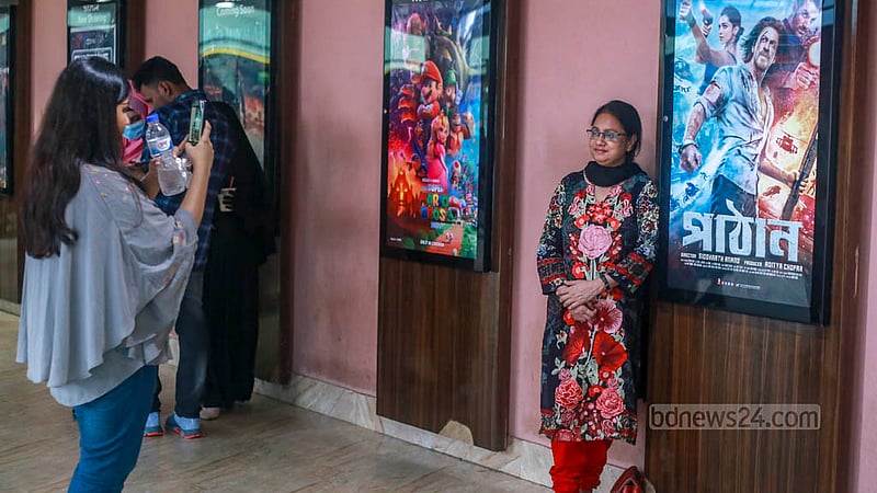 ঢাকার সিনেমা হলে ‘পাঠান’ সিনেমার পোস্টারের সাথে ছবি তুলছেন শাহরুখ ভক্তরা।&amp;nbsp;ছবি: তাওহীদুজ্জামান তপু