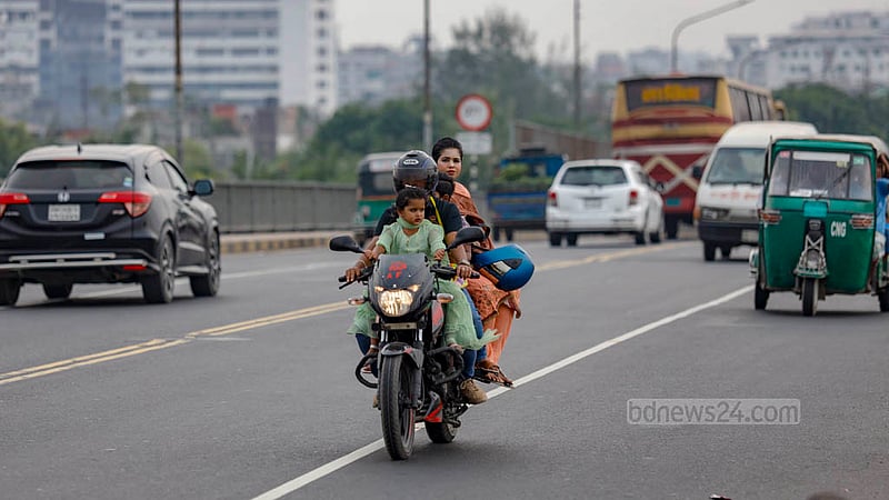 ঢাকার পোস্তগোলা সেতুর উপর দিয়ে দুই শিশুকে নিয়ে চলছেন এ মোটরসাইকেল চালক। চালকের মাথায় রয়েছে হেলমেট; তবে আরোহী নারীর হেলমেটটি হাতে আর দুই শিশুর মাথা অরক্ষিত, বসেছেও কোনো রকমে।&amp;nbsp;ছবি: মাহমুদ জামান অভি