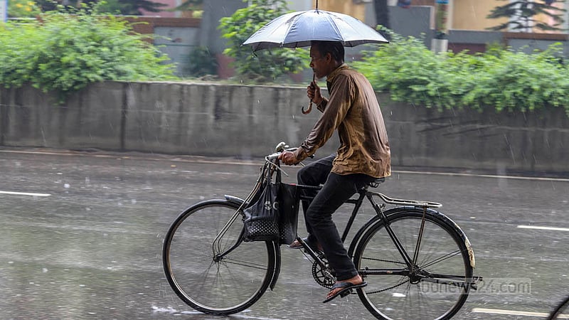 শ্রাবণের হঠাৎ বৃষ্টিতে বুধবার মিরপুরে ছাতা হাতে সাইকেলে একজন। আসিফ মাহমুদ অভি