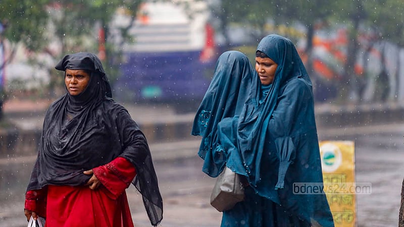 বৃষ্টির মধ্যে ভিজছেন মা; বৃষ্টি থেকে বাচাঁতে সন্তানকে বোরকা দিয়ে আগলে রেখে হেঁটে চলছেন তিনি।&amp;nbsp;ছবি: মাহমুদ জামান অভি