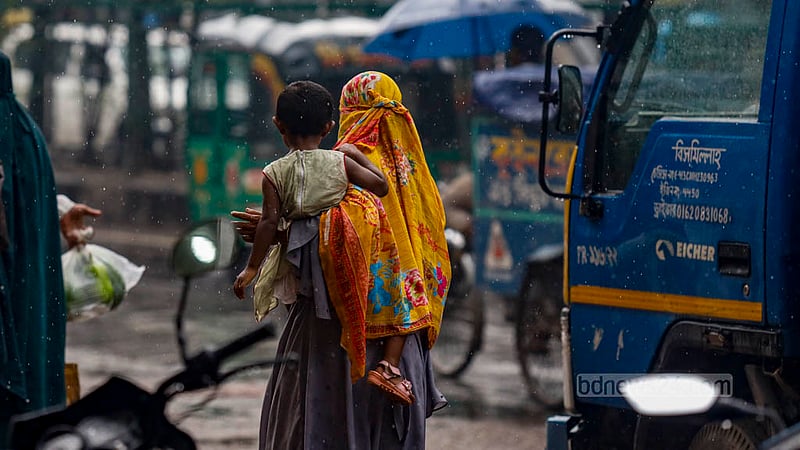 ঢাকার সবুজকানন এলাকায় মঙ্গলবার দুপুরে বৃষ্টির মধ্যে শিশু কোলে এক নারী।&amp;nbsp;ছবি: মাহমুদ জামান অভি