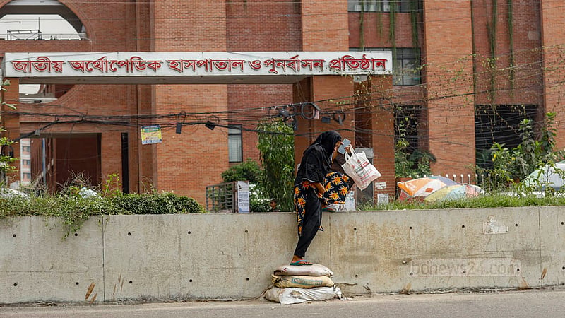 সড়ক বিভাজকের উচ্চতা অনেক, কয়েকটি বালুর বস্তা দিয়ে উপরে উঠতে ও নামতে হচ্ছে জাতীয় অর্থোপেডিক হাসপাতাল থেকে বের হওয়া এক নারীকে।&amp;nbsp;ছবি: মাহমুদ জামান অভি