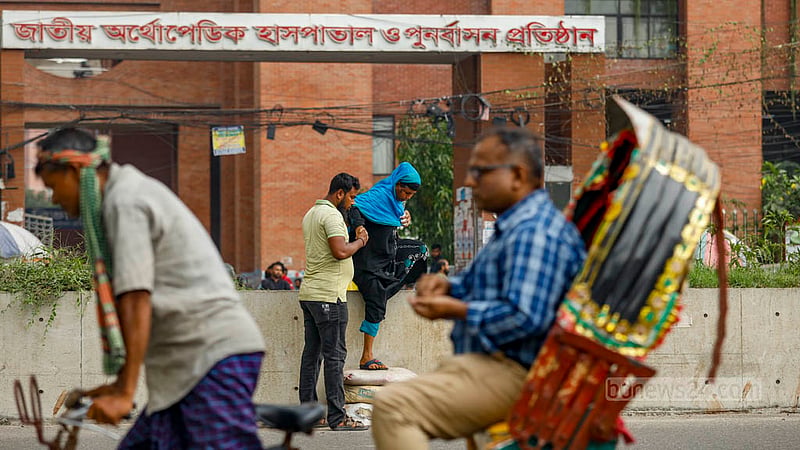 সড়ক বিভাজকের উচ্চতা অনেক, কয়েকটি বালুর বস্তা দিয়ে উপরে উঠতে ও নামতে হচ্ছে জাতীয় অর্থোপেডিক হাসপাতাল থেকে বের হওয়া এক নারীকে।&amp;nbsp;ছবি: মাহমুদ জামান অভি