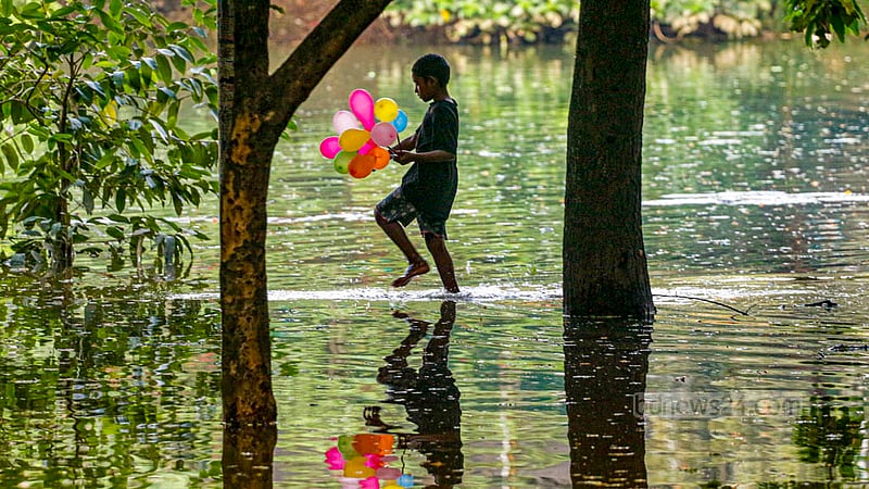 ঢাকার ধানমন্ডির লেক তলিয়ে গেছে পানিতে। উপচে পড়া পানিতে লেকের পাশের ওয়াকওয়ে ধরে বেলুন হাতে হেঁটে যাচ্ছে এক শিশু।