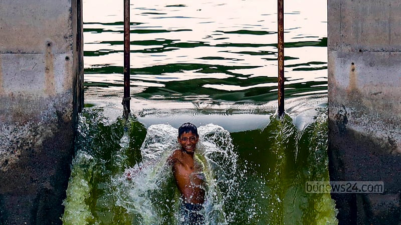 ঢাকার হাতিরঝিলের রামপুরা ব্রিজ অংশের খোলা স্লুইচ গেইট দিয়ে পানি বের হচ্ছে, আর তার মধ্যে গোসল করছে এক শিশু।
