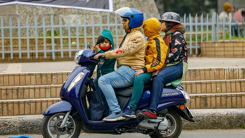 ঢাকা বিশ্ববিদ্যালয় এলাকায় একটি স্কুটারে চারজন, সবারই পা থেকে মাথা পর্যন্ত শীতের পোশাকে ঢাকা।