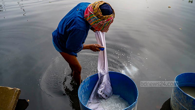 ঢাকার কামরাঙ্গীরচরে বুড়িগঙ্গার পানিতে হাঁটুজলে নেমে ড্রামের মধ্যে গুঁড়ো সাবান দিয়ে কাপড় পরিষ্কার করছেন এক ধোপা।