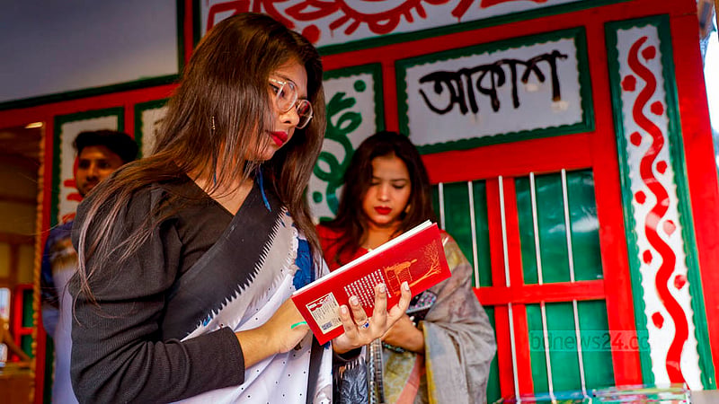 সোহরাওয়ার্দী উদ্যানে বইমেলার স্টলে বই দেখছেন দুই নারী।