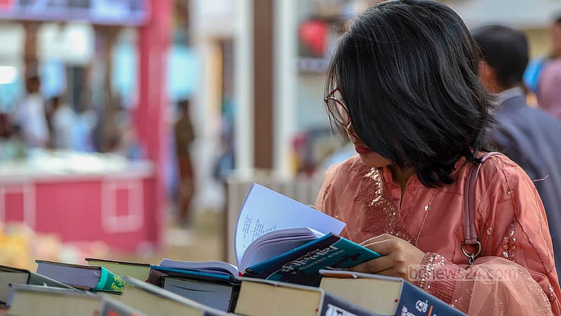 সাপ্তাহিক ছুটির দিন শনিবার বইমেলার স্টলে বই দেখছেন এক তরুণী।