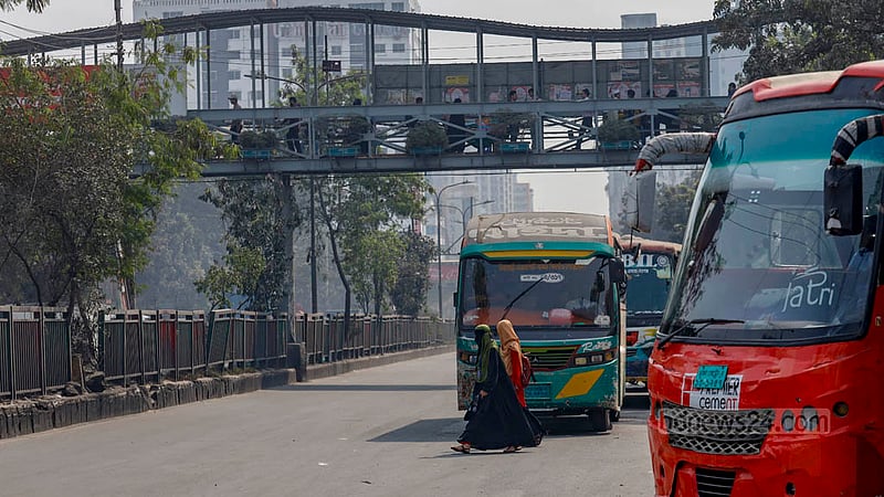 মাথার উপরে ফুটব্রিজ কিন্তু তারপরও ব্যস্ত নতুন বাজার এলাকায় চলন্ত বাসের সামনে দিয়ে পার হচ্ছেন দুই নারী।