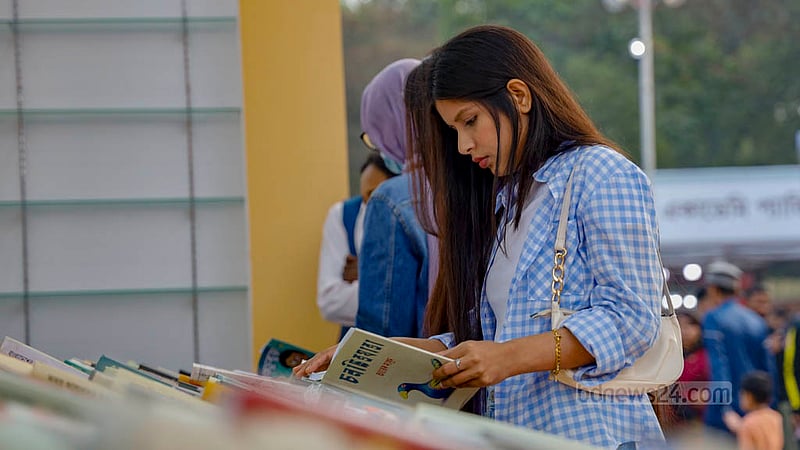 সাপ্তাহিক ছুটির দিন শুক্রবার বইমেলার স্টলে বই দেখছেন এক নারী।