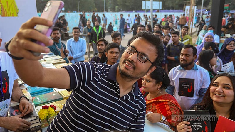 একুশে বইমেলার সোহরাওয়ার্দী উদ্যান অংশে একটি স্টলে পাঠকদের সঙ্গে ছবি তুলছেন লেখক সাদাত হোসাইন।