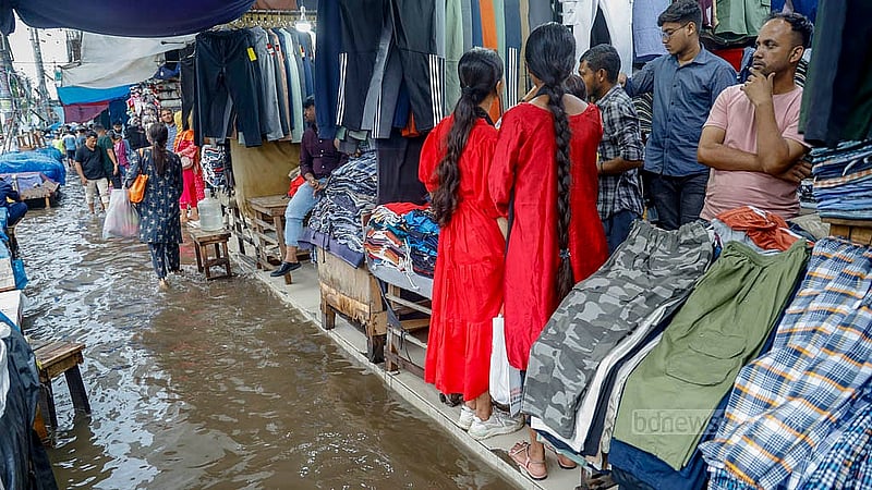 জলাবদ্ধ ধানমন্ডি হকার্স মার্কেটের ফুটপাতে একটি দোকানে পানির মধ্যে কেনাকাটা করতে দেখা যাচ্ছে ক্রেতাদের