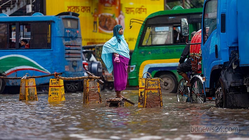 ঢাকার মিরপুর ১০ নম্বরে রোববার সকালে টানা বৃষ্টিতে ডুবে যাওয়া সড়কে কংক্রিটের উপরে দাঁড়িয়ে বাসে উঠার চেষ্টায় এক নারী
