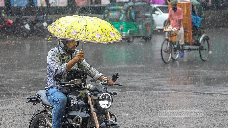 মৌসুমি বায়ুর প্রভাবে বুধবার দুপুরের বৃষ্টিতে ছাতা হাতে মোটরসাইকেল চালাতে দেখা যায় এক ব্যক্তিকে