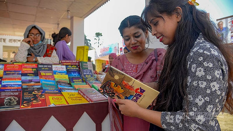 সোহরাওয়ার্দী উদ্যানে বইমেলার স্টলে বই দেখছেন দুই নারী।