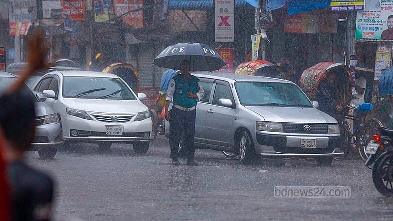 ঢাকার মোহাম্মদপুর বাসস্ট্যান্ড এলাকায় সোমবার দুপুরে ঝুম বৃষ্টির মধ্যে ছাতা হাতে ট্রাফিক নিয়ন্ত্রণে এক পুলিশ সদস্য