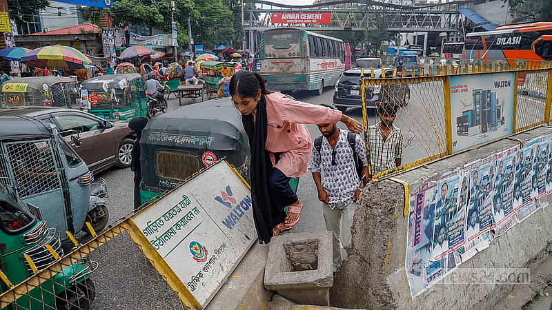 ঢাকার মহাখালীতে সড়ক বিভাজকের উপরে দেওয়া লোহার বেষ্টনীর ফাঁক দিয়ে ঝুঁকি নিয়ে সড়ক পার হচ্ছেন এক নারী