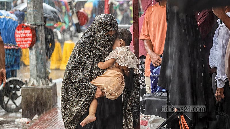 বৃষ্টির মধ্যে শিশু সন্তানকে নিয়ে নিরাপদ আশ্রয়ে যান এক নারী; ঢাকার দোলাইরপাড় থেকে তোলা