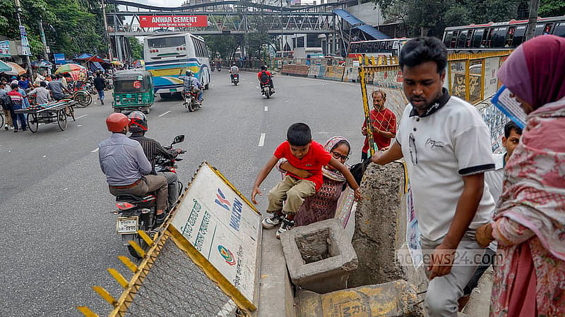 ঢাকার মহাখালীতে সড়ক বিভাজকের উপরে দেওয়া লোহার বেষ্টনীর ফাঁক ঠেলে এক শিশুকে তুলছেন এক নারী