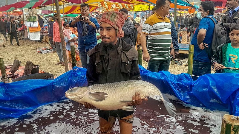 ঐতিহ্যবাহী পোড়াদহ মেলার একটি স্টলে চৌবাচ্চার ভেতরে একটি মাছ হাতে তুলে ক্রেতার দৃষ্টি আকর্ষণের চেষ্টায় এক বিক্রেতা