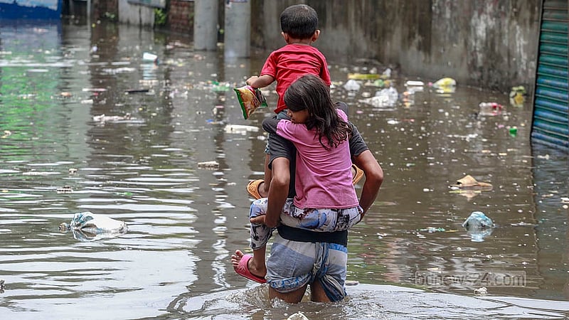 ঢাকার সায়েদাবাদে মঙ্গলবার দুপুরে দুই সন্তানকে কাঁধে তুলে জলাবদ্ধ সড়ক পার হচ্ছেন এক বাবা