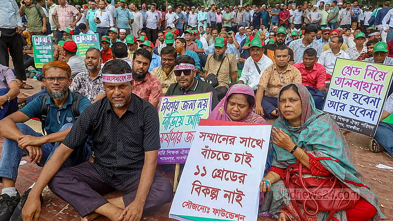 তিন দাবি আদায়ে ঢাকায় কেন্দ্রীয় শহীদ মিনার প্রাঙ্গণে ‘প্রাথমিক সহকারী শিক্ষক সংগঠন ঐক্য পরিষদের’ মহাসমাবেশে প্ল্যাকার্ড হাতে শিক্ষকরা