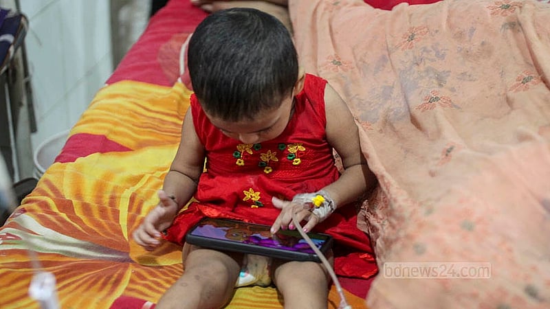 মোবাইল ফোনে সময় কাটছে ডেঙ্গু আক্রান্ত শিশুর। মঙ্গলবার ঢাকার মুগদা জেনারেল হাসপাতালের শিশু ওয়ার্ডে