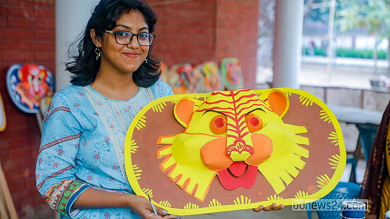 পহেলা বৈশাখ উদযাপনে ঢাকা বিশ্ববিদ্যালয়ের চারুকলা অনুষদে কাগজের মুখোশ রঙ করা শেষে দেখাচ্ছেন এক শিক্ষার্থী