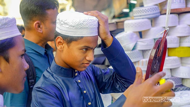 ঢাকায় বায়তুল মোকাররম মসজিদের সামনে একটি দোকানে মাথায় টুপি পরে পরখ করে নিচ্ছেন এক ক্রেতা।  ছবি: আব্দুল্লাহ আল মমীন