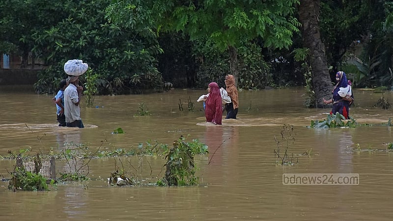 ফেনীর ফাজিলপুরে ডুবে থাকা সড়কে কোমরপানি পেরিয়ে আশ্রয়ের সন্ধানে বাসিন্দারা। ছবি: সুমন বাবু