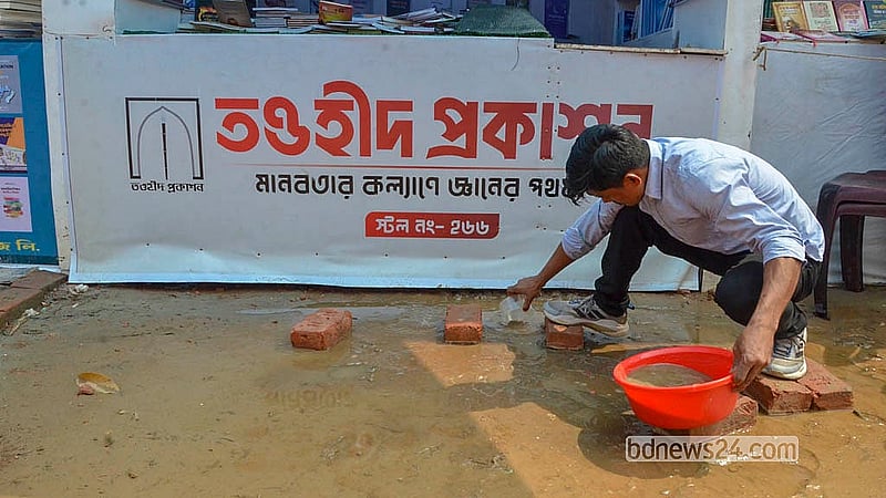 সোহরাওয়ার্দী উদ্যান বইমেলা প্রাঙ্গণে স্টলের সামনে জমে থাকা পানি সরাচ্ছেন এক দোকানি।