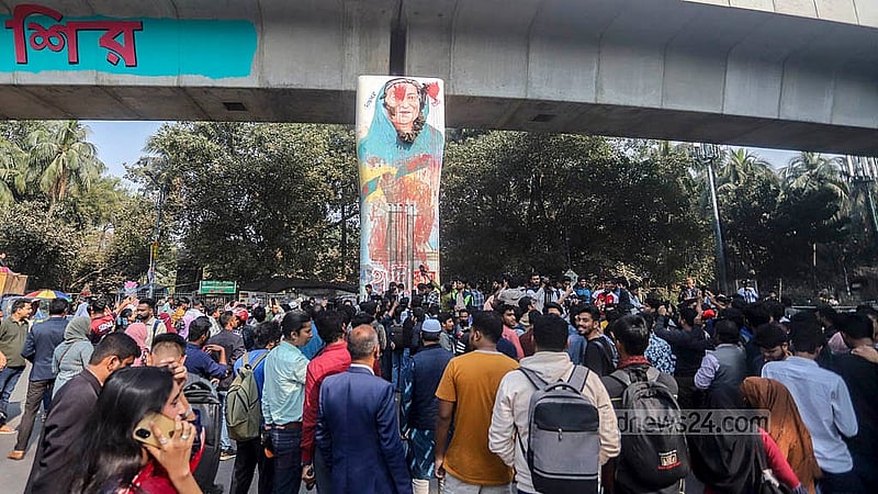 ঢাকা বিশ্ববিদ্যালয়ের রাজু ভাস্কর্য সংলগ্ন মেট্রোরেলের পিলারে সাবেক প্রধানমন্ত্রী শেখ হাসিনার প্রতিকৃতিতে জুতা নিক্ষেপ করা দেখে ভিড় করেন আশেপাশের মানুষ। ছবি: আব্দুল্লাহ আল মমীন