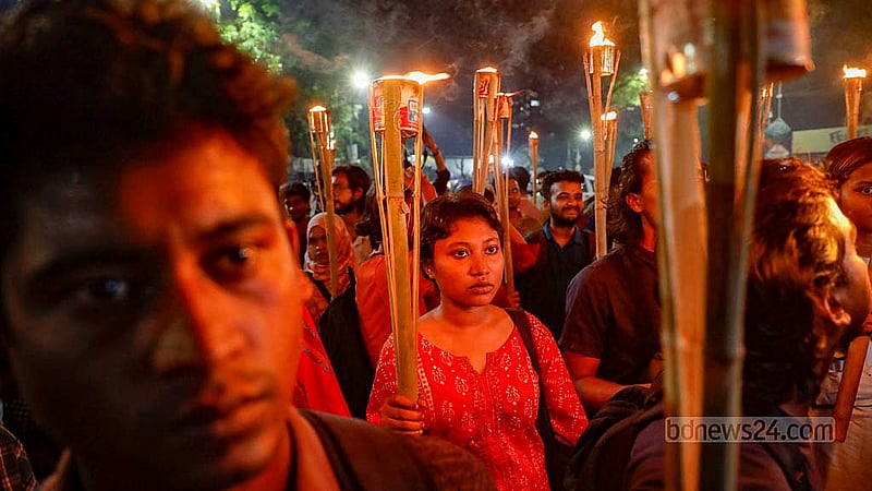 মশাল হাতে ধর্ষণ ও নারী নির্যাতনের প্রতিবাদে বৃহস্পতিবার রাতে ঢাকা বিশ্ববিদ্যালয়ের রাজু ভাস্কর্যের সামনে এক নারী। ছবি: মাহমুদ জামান অভি