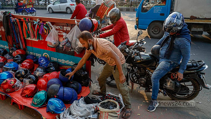 রাজধানীর সায়েন্সল্যাব মোড়ে ফুটপাতের দোকানের পাশে মোটারসাইকেল থামিয়ে হেলমেট দেখছেন এক চালক