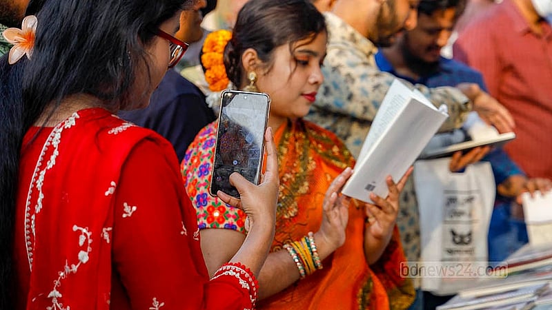 বই কেনার জন্য নয়, বই হাতে পড়ার ভঙ্গিমায় স্টলে ছবি তোলার জন্যও বইমেলায় আসা। ছবি: মাহমুদ জামান অভি