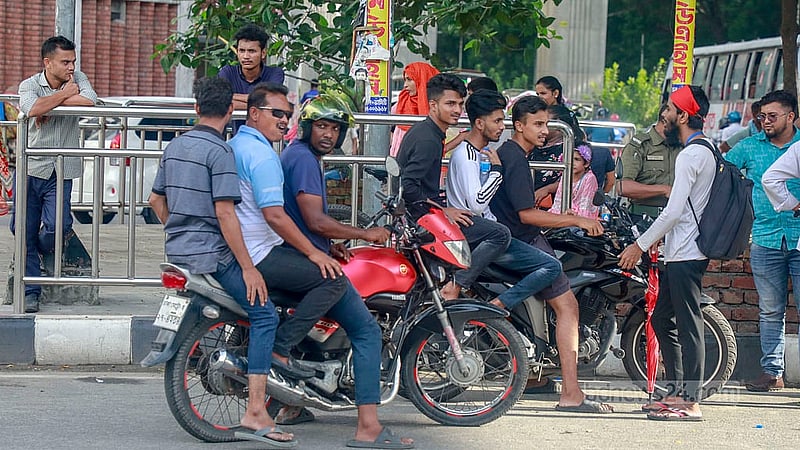 দুই মোটরসাইকেলে চেপেছেন তিনজন করে। পাঁচজনের মাথায়ই নেই হেলমেট। বিজয় সরণী মোড়ে তাদেরকে থামিয়ে বোঝানোর চেষ্টা করছেন শিক্ষার্থীরা।